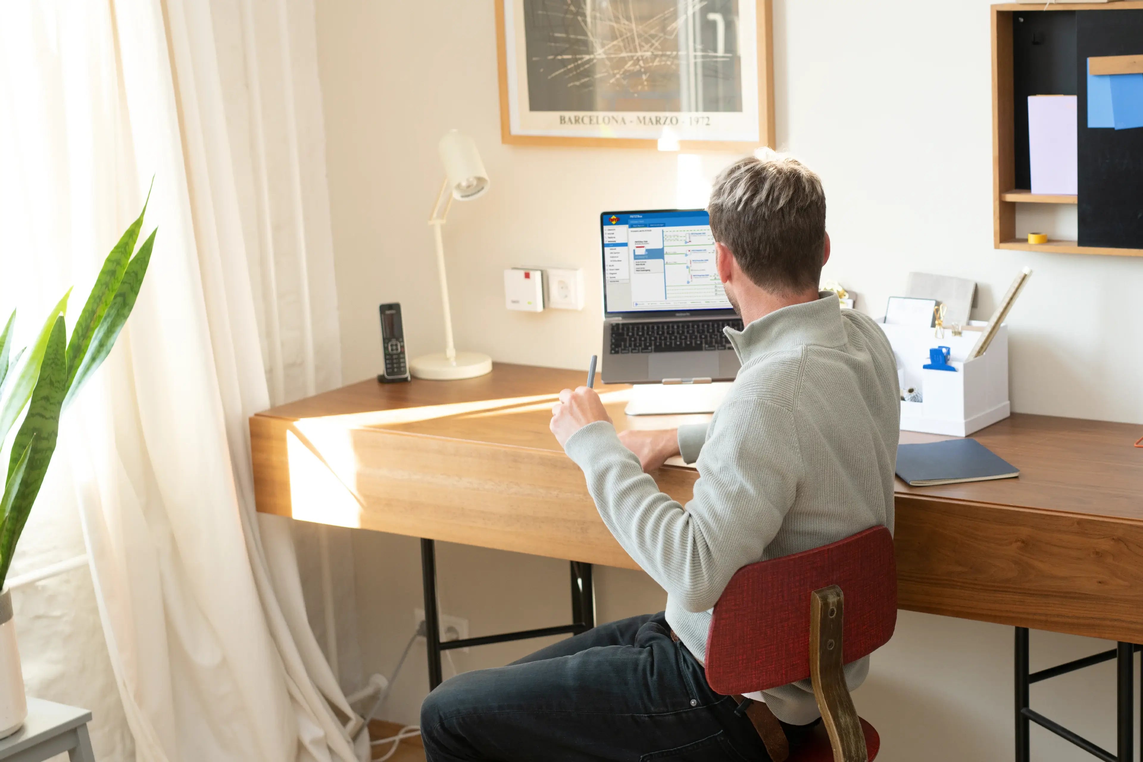 Mann sitzt am Schreibtisch, arbeitet am Laptop in einem hellen, modernen Raum mit Pflanzen.