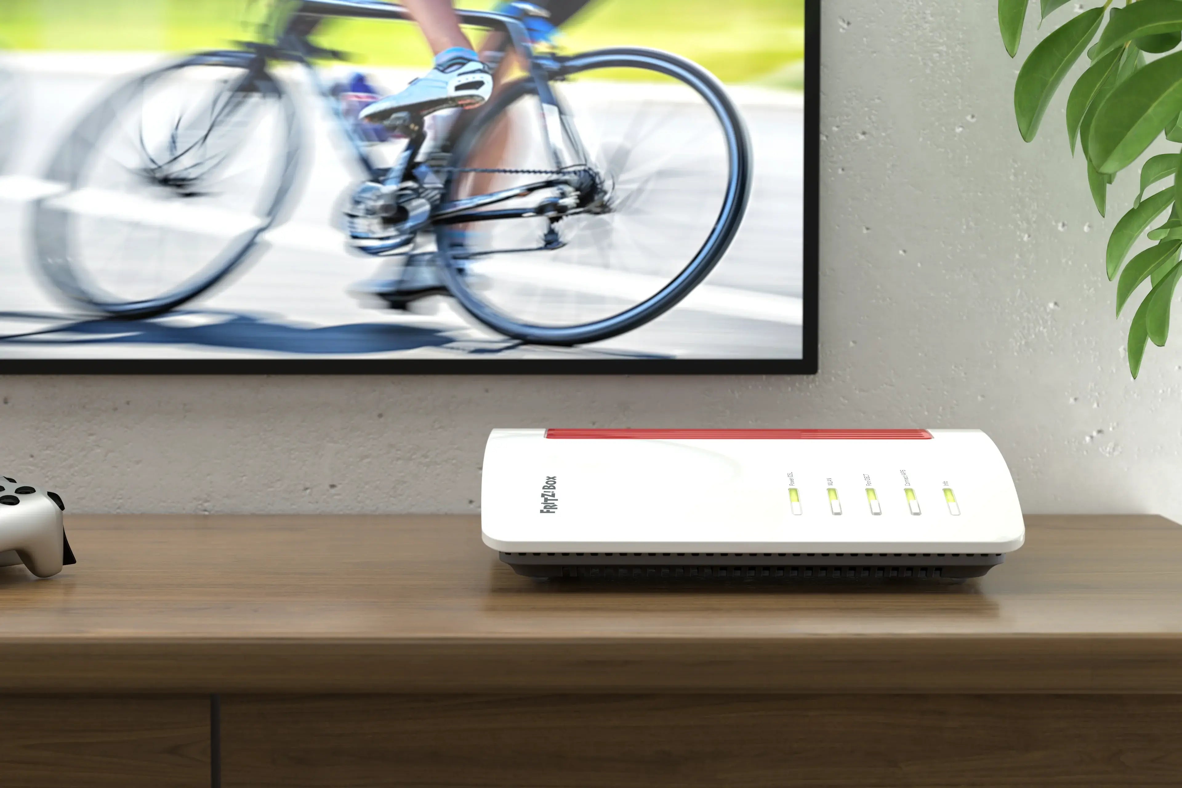 Ein Router auf einem Tisch mit einem Fernseher im Hintergrund, der einen Radfahrer zeigt.